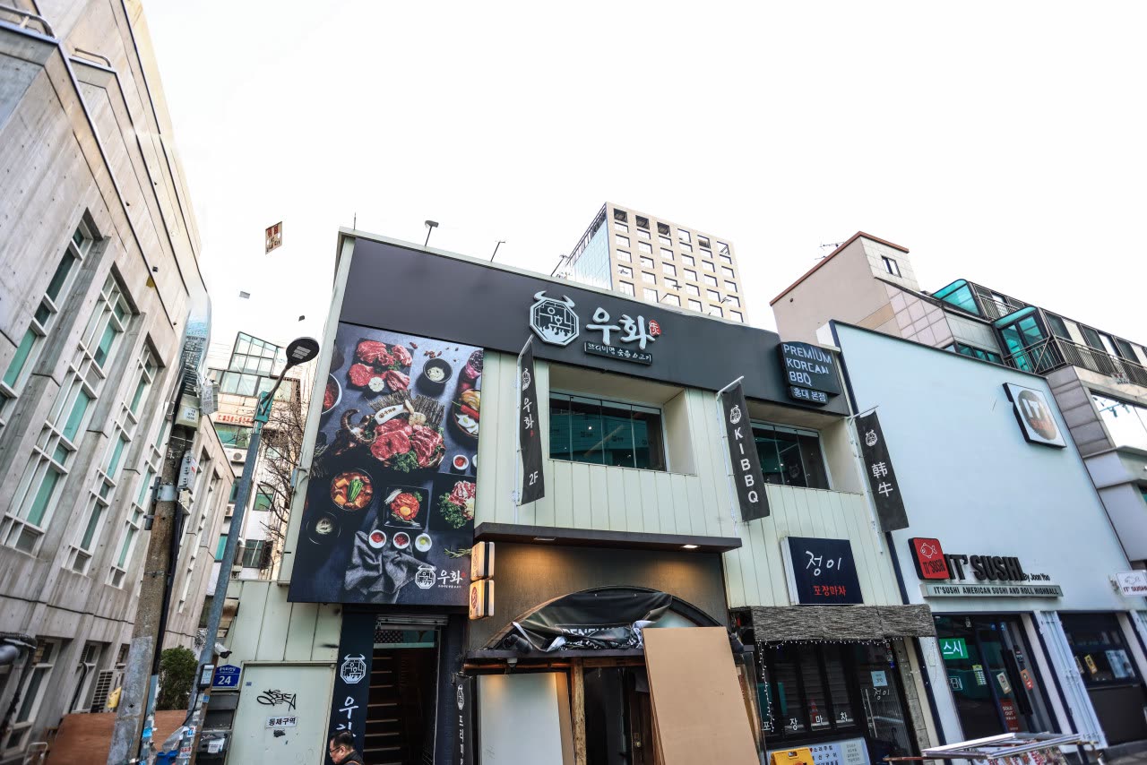 홍익로5안길 골목에서 올려다본 건물. 우화 홍대본점이 들어선 2층 간판이 보이고, 양옆으로 다른 가게들의 간판이 이어진다